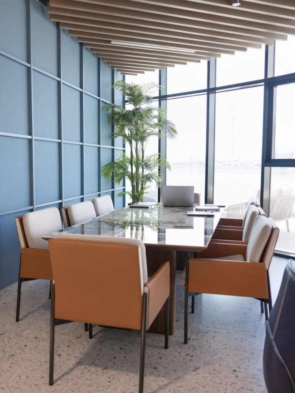Empty small business meeting room with table and eight seats, full length of chairs, stone surface of desk, blue wall, large window and potted plant for workspace interior decoration