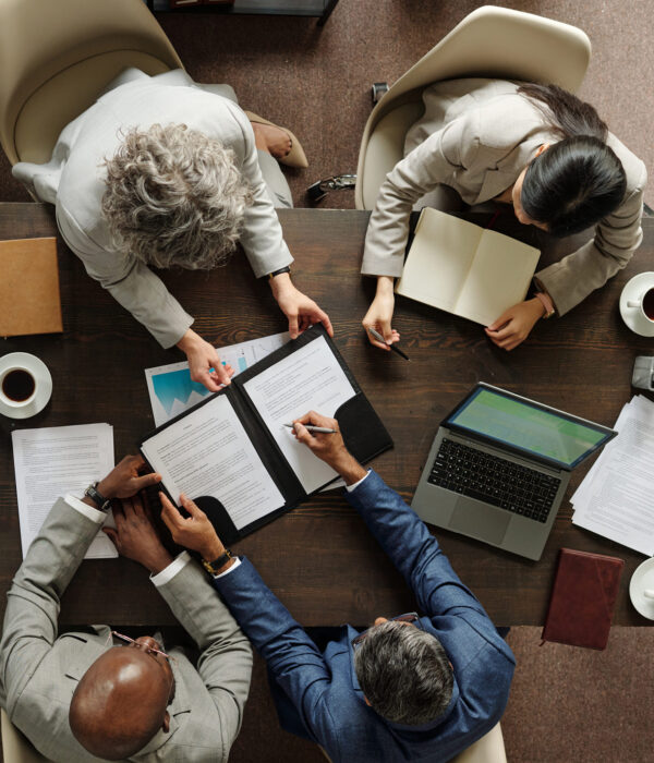Group of middle aged multiethnic business professionals collaborating around table, reviewing documents and using laptop, top view showing teamwork and corporate meeting environment